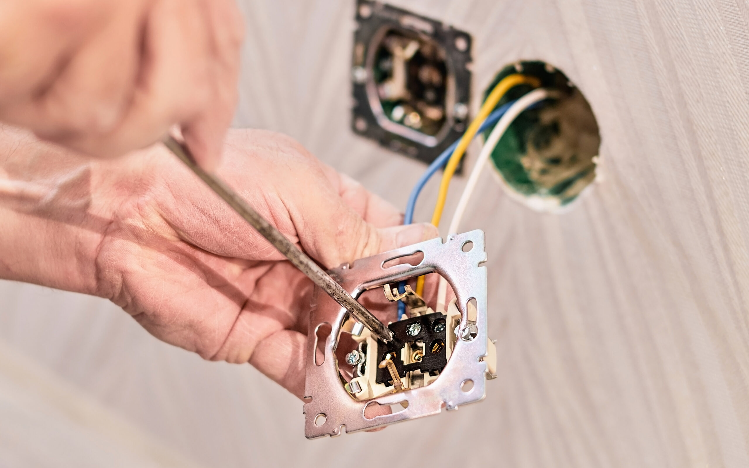 Hands of an electrician installing an electrical outlet in a new house. Assembly of the electrical network in the room, installation of the electrical network